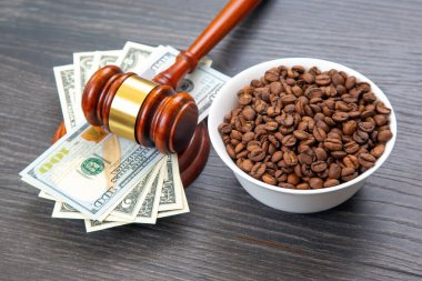 Tahta bir yüzeyde bir kase kahve çekirdeğinin yanında duran 100 dolarlık banknotlar, finans ve tarım alanlarındaki yasal ve ticari kavramları temsil ediyor..