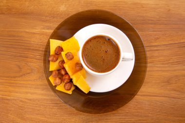 Beyaz espresso bardağının sade ama zarif bir kompozisyonu. Bir tabağın üzerinde kremalı köpük bir kapak ile, ahşap bir masanın üzerindeki sarı peynir dilimleri ile tamamlanmış..