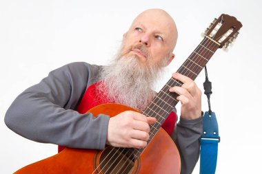 Uzun beyaz sakallı kel yaşlı bir adam akustik gitar çalar, kırmızı ve gri atletik bir gömlek giyer, beyaz bir arka planda izole edilmiş, bir müzik anı yakalar..