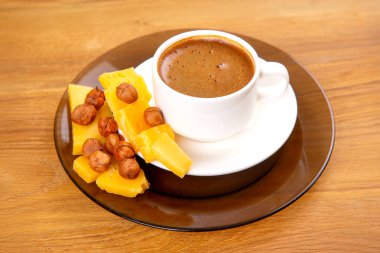 Beyaz espresso bardağının sade ama zarif bir kompozisyonu. Bir tabağın üzerinde kremalı köpük bir kapak ile, ahşap bir masanın üzerindeki sarı peynir dilimleri ile tamamlanmış..