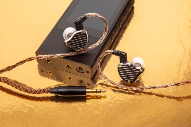 Parlak altın bir yüzeye karşı siyah bir ses cihazına yerleştirilmiş örgülü kabloyla, zarif kablo kulaklıklar. Müzik, teknoloji ve yaşam tarzı fotoğrafçılığına uygundur.
