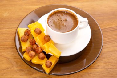 Beyaz fötr bir fincanın düz resmi köpükle demlenmiş espresso, sarı peynir dilimlerinden oluşan bir yelpazenin yanında, doğal ahşap bir yüzey üzerine kurulmuş bir fincan..