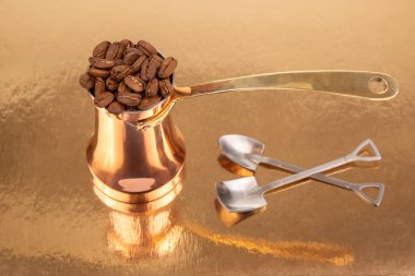 Altın bir yüzey üzerinde kahve çekirdeği yığını ile birlikte pirinç saplı cilalı bakır bir mağara, geleneksel kahve demleme ve yaşam tarzı temaları için mükemmel.