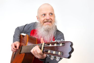 Büyük kel adam, kalın gri sakallı ahşap bir gitar çalar, kırmızı ve gri bir spor gömlek giyer, temiz beyaz bir zemine karşı kurulur, tutkulu bir performans sergiler..