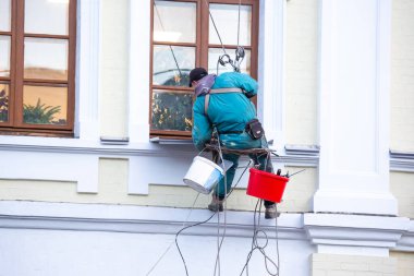 Camları temizleyen dağcı işçisi ve yenilenmiş bir konut binasının ön cephesi. inşaat sektörü