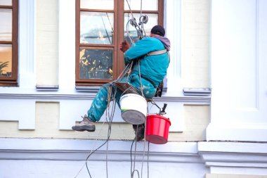 Camları temizleyen dağcı işçisi ve yenilenmiş bir konut binasının ön cephesi. inşaat sektörü