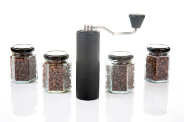 Kahve çekirdekleri için siyah manuel kahve öğütücüsü ve siyah kahve çekirdekleri ile dolu dört cam şeffaf kavanoz ve beyaz arka planda kahve demlemek için toprak takımı..