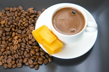 Koyu bir yüzeyde beyaz bir fincanda espresso, peynir çubukları ve kahve çekirdekleri gibi nefis bir düzenleme, bir gurme anını yakalıyor..