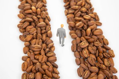 Kahve çekirdekleri arasında yürüyen takım elbiseli küçük bir heykelciğin yer aldığı eşsiz stok fotoğrafı kahve pazarındaki bir iş yolunu gösteriyor.