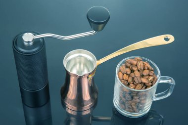 Metalik saplı siyah manuel kahve öğütücüsü, altın saplı bakır bir çakmak ve parlak siyah bir yüzey üzerinde cam bardak, kahve demleme seansları için ideal.