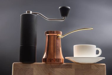 Siyah bir el değirmeni, bakır bir kahve makinesi ve çay tabağı olan beyaz fincan, koyu mavi arka planda, kahve demleme seansları için mükemmel..