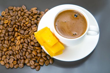 Koyu bir masada peynir çubukları ve kahve çekirdekleri olan beyaz bir fincan espresso yemek sevenlere kırsal ve manzaralı bir bakış açısı sunuyor.