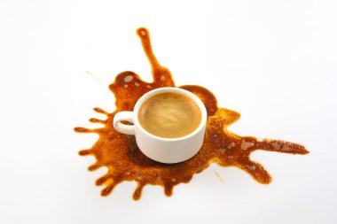 Beyaz bir kahve fincanı el değmemiş bir yüzeye oturur ve dışa doğru yayılan kahverengi bir kahve lekesi sanatsal bir model oluşturur. Koyu espresso temiz arka planla çok güzel zıtlaşıyor.