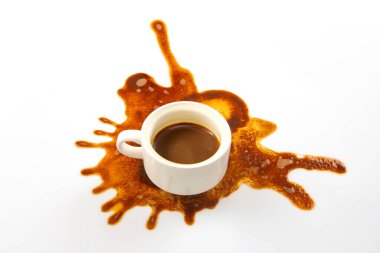 Beyaz bir kahve fincanı el değmemiş bir yüzeye oturur ve dışa doğru yayılan kahverengi bir kahve lekesi sanatsal bir model oluşturur. Koyu espresso temiz arka planla çok güzel zıtlaşıyor.