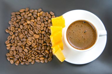 Beyaz espresso bardağının yakın çekimi, peynir çubukları, ve kahve çekirdekleri karanlık bir masada, basit ama zarif bir yemek eşleşmesi sergiliyor..