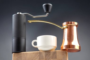 Modern bir manuel kahve öğütücüsü, bakır Türk çakmağı, ve ahşap bir yüzey üzerinde beyaz seramik bardak, sıcak bir kahve havası için koyu mavi arka planda yakalanmış.. (