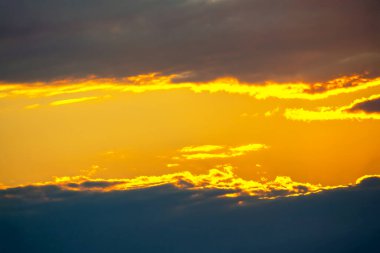 Turuncu, sarı ve koyu mavi tonlarında dramatik bulut oluşumlarıyla gün batımı. Işık ve gölge oyunu büyüleyici bir doğal bileşim yaratır..