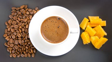 Kahve fincanında beyaz bir fincanda espresso, peynir çubukları ve kahve çekirdekleri koyu bir yüzeye yayılmış, sıcak bir sabah titreşimini vurguluyor..