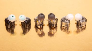 Parlak altın bir arka planda sergilenen siyah, gümüş ve açık renkli kulaklıklar. Teknoloji, müzik ve modern tasarım kavramları için mükemmel..