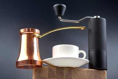 Pürüzsüz, siyah bir kahve öğütücüsünün yakın plan çekimi, geleneksel bakır çakmak, ve ahşap bir tahtanın üzerinde beyaz bir kupa, kahve fotoğrafçılığı için şık, koyu mavi bir zemin üzerine kurulmuş.