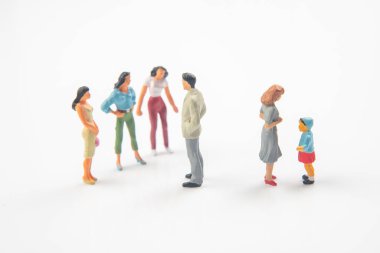 Yetişkinler ve elinde top olan bir çocuk da dahil olmak üzere iki renkli minyatür heykel grubu, sosyal uzaklığı, aileyi veya toplum dinamiğini sembolize eden yansıtıcı beyaz bir yüzey üzerinde ayrı dururlar..