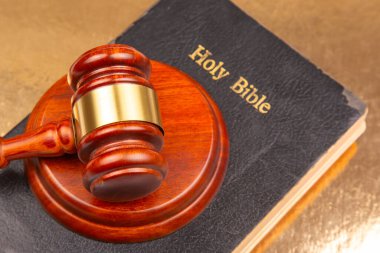 Altın bir yüzey üzerinde altın bir şerit bulunan ahşap bir tokmak, hukukun, inancın ve yargının kesişimini sembolize ediyor..