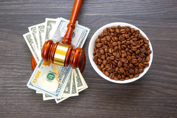 Tahta tokmağın tepesinde 100 dolarlık banknotlar var. Koyu ahşap bir arka planda kavrulmuş kahve çekirdekleri. Adalet ve ticareti sembolize ediyor.