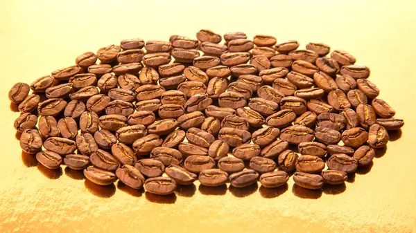 Kavrulmuş kahve çekirdekleri parlak altın bir zemin üzerinde oval bir yapı oluşturarak koyu kahverengi renklerini ve pürüzsüz dokularını ön plana çıkarırlar. Yiyecek ve içecek imgeleri için ideal..