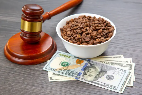 Tahta bir masada, 100 dolarlık banknotlar üzerinde bir tokmak ve bir kase kahve çekirdeği adalet, finans hukuku ve küresel kahve ticareti temalarını çağrıştırıyor..