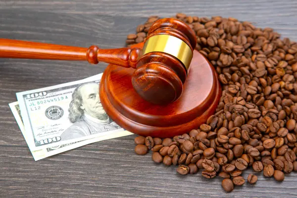 Tahta bir tokmak, koyu ahşap bir yüzey üzerinde 100 dolarlık bir banknotun yanında duran kahve çekirdekleri, hukuk, finans ve ticaretin kesişimini sembolize ediyor. Yasal, ticari veya ticari temalar için ideal