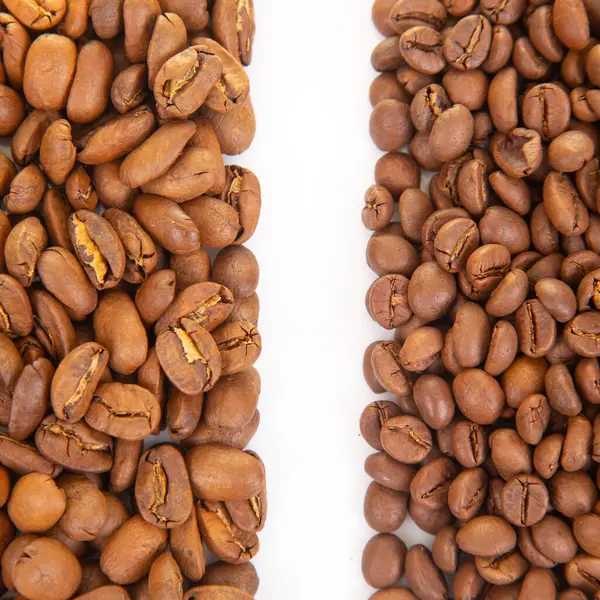 Kavrulmuş kahve çekirdeklerini yakın plan beyaz zemin üzerinde iki tonda, toprak renklerini ve çatlak yüzeylerini vurgulayarak. Gurme kahve görselleri için mükemmel.