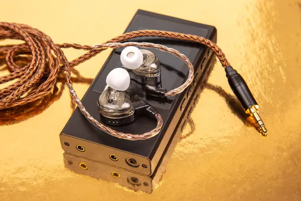 Parlak, siyah bir ses oynatıcının üzerinde dokuma kablosu olan kablolar, yansıtıcı altın bir yüzeye kurulmuş. Teknoloji, ses ve modern tasarım kavramları için ideal.