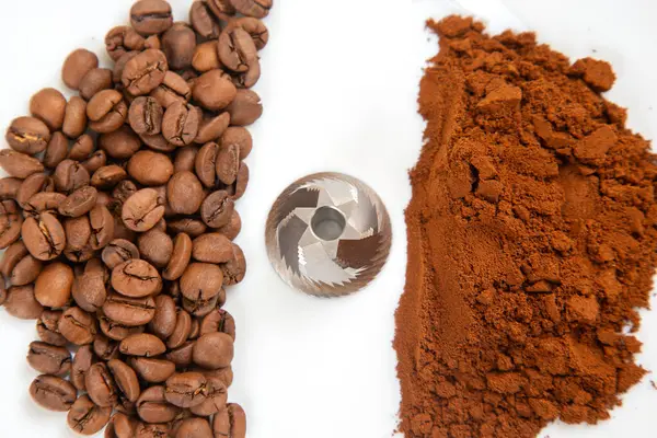 Kahve çekirdekleri, öğütücü ve öğütme işlemini vurgulamak için beyaz bir yüzeyde öğütülmüş kahve tozu. Kahve kültürü tasvirleri için harika..