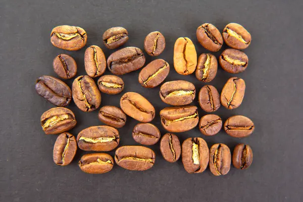 Kavrulmuş kahve çekirdeklerinin detaylı görüntüsü, koyu arkaplandaki sıcak kahverengi gölgeleri ve doğal çatlakları vurguluyor. Kafeinle ilgili projeler için uygundur.