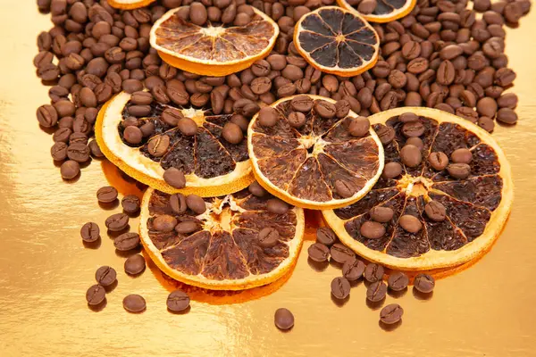 Kavrulmuş kahve çekirdekleri ve altın yansıtıcı bir tabanda kurutulmuş portakal dilimleri, dış görünüş ve sıcaklık. Kahve aroması ve turunçgiller.