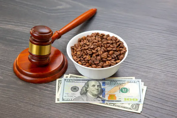 Tahta bir tokmak, siyah ahşap bir yüzeyde kavrulmuş kahve çekirdeğinin yanında adaleti ya da yasal masrafları sembolize eden 100 dolarlık banknotlar yığınının üzerinde duruyor. Hukuk ve ticaret kavramı.