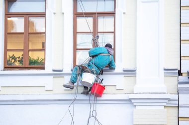 Camları temizleyen dağcı işçisi ve yenilenmiş bir konut binasının ön cephesi. inşaat sektörü