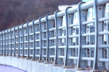 Çağdaş metal bir köprüye yakın plan, yatay demir parmaklıklar ve cıvatalar, bulanık doğal bir arka plan üzerine kurulmuş. Gösterişli tasarım ve endüstriyel his onu mimari için ideal kılıyor.