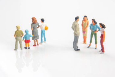 Yetişkinler ve elinde top olan bir çocuk da dahil olmak üzere iki renkli minyatür heykel grubu, sosyal uzaklığı, aileyi veya toplum dinamiğini sembolize eden yansıtıcı beyaz bir yüzey üzerinde ayrı dururlar..