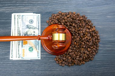 Hukuki ve finansal temalar, bir tokmağın kırsal bir ahşap yüzey üzerindeki 100 dolarlık banknotun yanında kahve çekirdeklerine dayanırken, kahve ticareti ve ekonomik adaleti ön plana çıkarırken çarpışıyor.