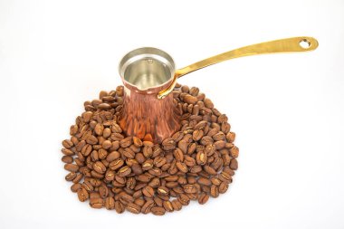 Pirinç saplı parlak bakır bir mağara, parlak beyaz bir yüzey üzerinde kahve çekirdekleri yığını, geleneksel kahve demleme ve yaşam tarzı temaları için mükemmel..