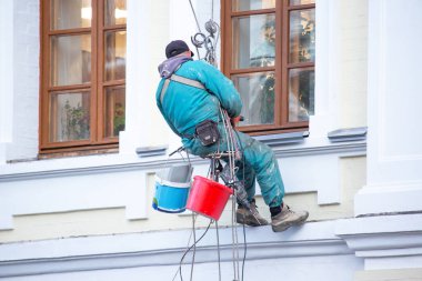 Camları temizleyen dağcı işçisi ve yenilenmiş bir konut binasının ön cephesi. inşaat sektörü