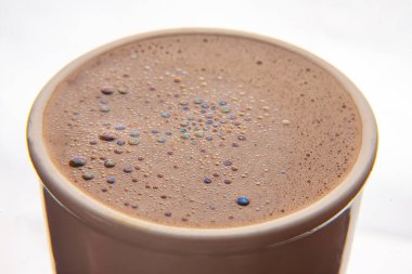 Seramik bir fincanda canlı, yanardöner kabarcıklar olan köpüklü bir kahve yüzeyinin yakın çekimi, zengin kahverengi bir doku ve büyüleyici ışık yansımaları sergiliyor..