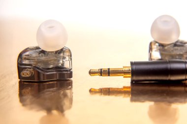 Beyaz uçlu zarif bir kulaklık, 3.5 mm 'lik bir fiş, ve parlak altın bir fon üzerinde siyah bir müzik çalar, teknoloji, ses ve modern tasarım fotoğrafçılığı için uygun..
