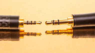 Yansıtıcı altın bir yüzey üzerinde altın konnektörlü 3.5 mm 'lik iki ses kriptosu, teknoloji ve ses ekipmanları teması için ideal