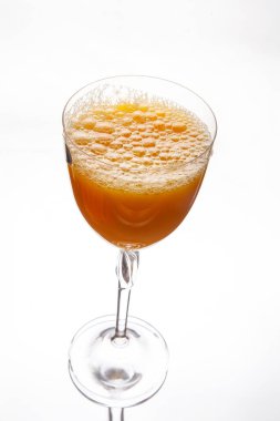 Ferahlatıcı bir bardak taze sıkılmış portakal suyu köpüklü bir üst, temiz beyaz arka planda zarif bir berrak şarap bardağında servis edilir. Yemek, içecek ve sağlıklı yaşam temaları için mükemmel..