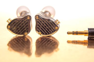Beyaz uçlu zarif bir kulaklık, 3.5 mm 'lik bir fiş, ve parlak altın bir fon üzerinde siyah bir müzik çalar, teknoloji, ses ve modern tasarım fotoğrafçılığı için uygun..