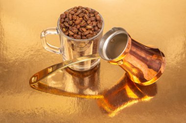 Pirinç saplı bakır bir kahve demliği ve altın kaplamalı kahve çekirdekleri ile dolu bir cam bardak. Mutfak için ideal.