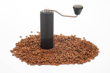 Metalik saplı bir el yapımı kahve öğütücüsü ve bir kase kahve çekirdeği, dağınık fasulyeli, ticari kullanım için parlak beyaz bir arka planda..