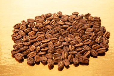 Sıcak tonlarını ve doğal dokularını ortaya çıkaran altın yansıtıcı arka planda kavrulmuş kahve çekirdekleri yığını. Kahve kültürü görselleri için mükemmel.